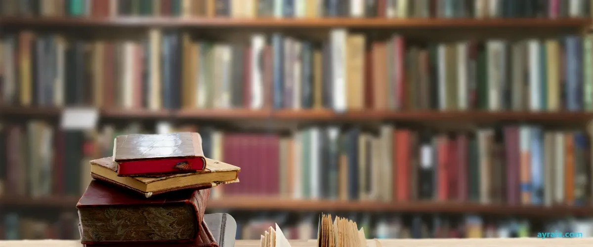 Stack of old, worn textbooks on a library table in front of blurred bookshelves